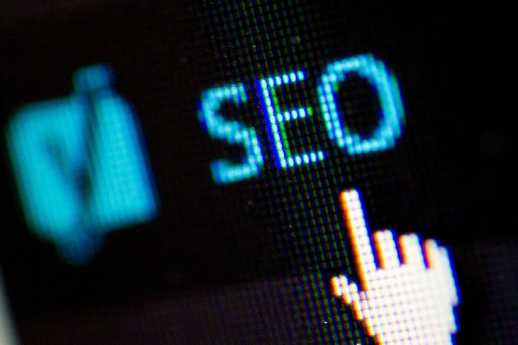 Gros plan d'un écran d'ordinateur affichant le texte « SEO » avec une apparence pixellisée. Un curseur pixellisé pointe vers le texte. À gauche, une icône floue ressemblant à une coche est visible.