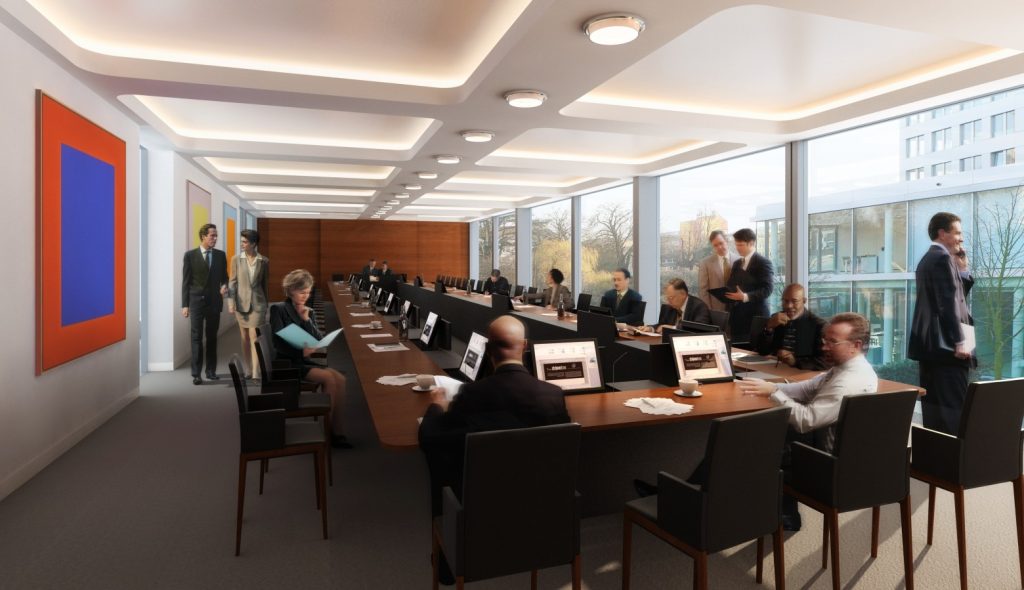 Une salle de conférence moderne avec une longue table rectangulaire entourée de personnes assises et de quelques personnes debout. La salle dispose de grandes fenêtres, de peintures abstraites colorées sur un mur et de plusieurs plafonniers. Les participants participent à diverses activités, notamment la lecture et la conversation.