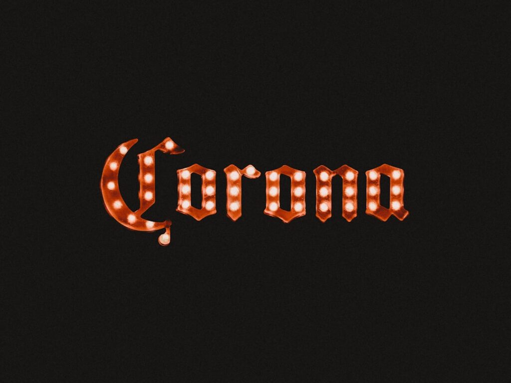 Panneau lumineux de style vintage affichant le mot « Corona » en lettres ornées d'ampoules sur un fond sombre.