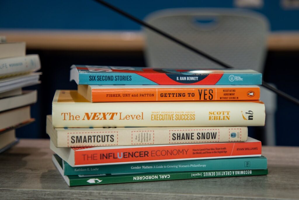 Une pile de sept livres sur une table, comprenant des titres comme « Getting to Yes », « The Next Level », « Smartcuts » et « The Influencer Economy ». Les livres se concentrent sur des sujets tels que la négociation, le succès et les stratégies de renforcement de l'influence.